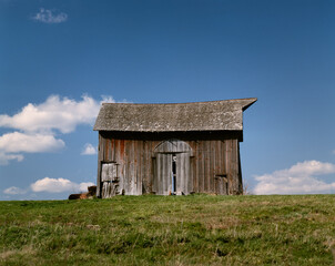 Obraz premium An old barn that was, at one time, red on a hillside in Adair County in Northeast Missouri with puffy clouds dotting the blue sky background. 1985