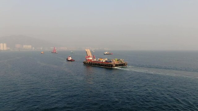 Barge loaded with Concrete mixer trucks pulled to port by a Tugboat in Hong Kong bay, Aerial view.