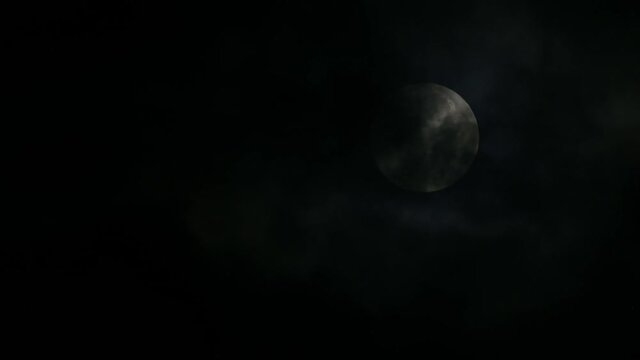 Moon almost in the middle of the right side of the frame partially covered by dark clouds, seen in the middle of a cold winter night in Kaeng Krachan National Park, Thailand.