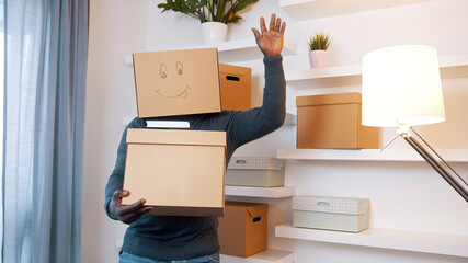 Fototapeta premium Happy young man with smiling cardboard box over his head dancing while moving in the new home. Purchase of new property. High quality photo