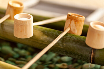 Purifying fountain at a Shinto Shrine in Japan. Image features unfinished wooden cups with long...
