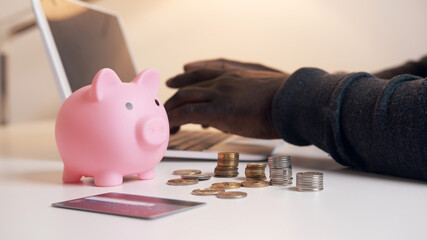Hands of black man working on the laptop behind piggybank and coins. Accounting and finances concept. High quality photo