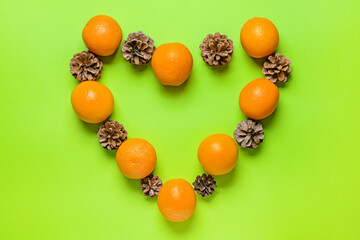 Heart made of oranges and pine cones on color background