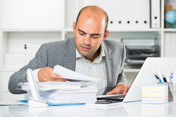 Young and smiling businessman in shirt viewing documents at the table