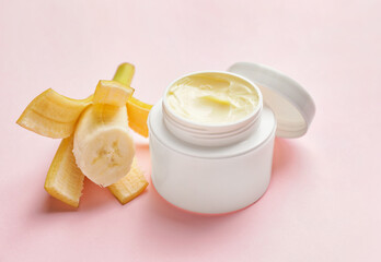 Jar of natural cream and fresh banana on color background