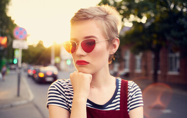Obraz premium fashionable woman with short hair in glasses and a sundress walks down the street in summer