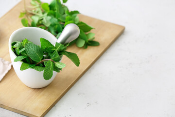 Mortar with mint and pestle on light table in kitchen