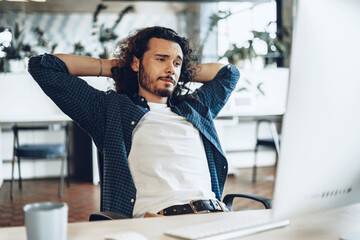 Young businessman sitting in office with hands behind his head satisfied with work done
