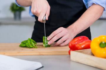 young male cutting a green bell pepper on a cutting board with a knife