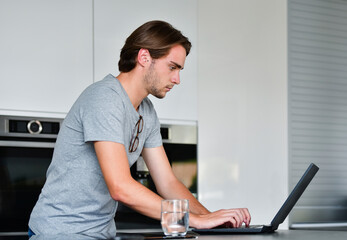 Side view of a focused handsome young man using a laptop on an out of focus background. Technology concept.