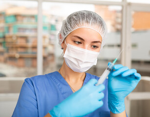 Female nurse or doctor wearing in face mask and medical uniform holding vial and syringe