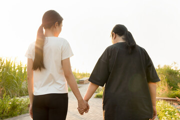 Senior mother walking hand in hand with daughter in urban park during summer time, concept of family love and care, mother day, family day, mom and daughter togetherness in pleasant urban summer