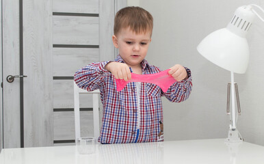 Little boy playing with pink slime at home. A fashionable liquid toy that stretches to the side....