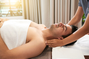 Calm handsome young man enjoying relaxing face, head and shoulders massage in spa salon