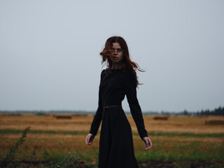A woman in a black dress walks in the field on nature in the evening model