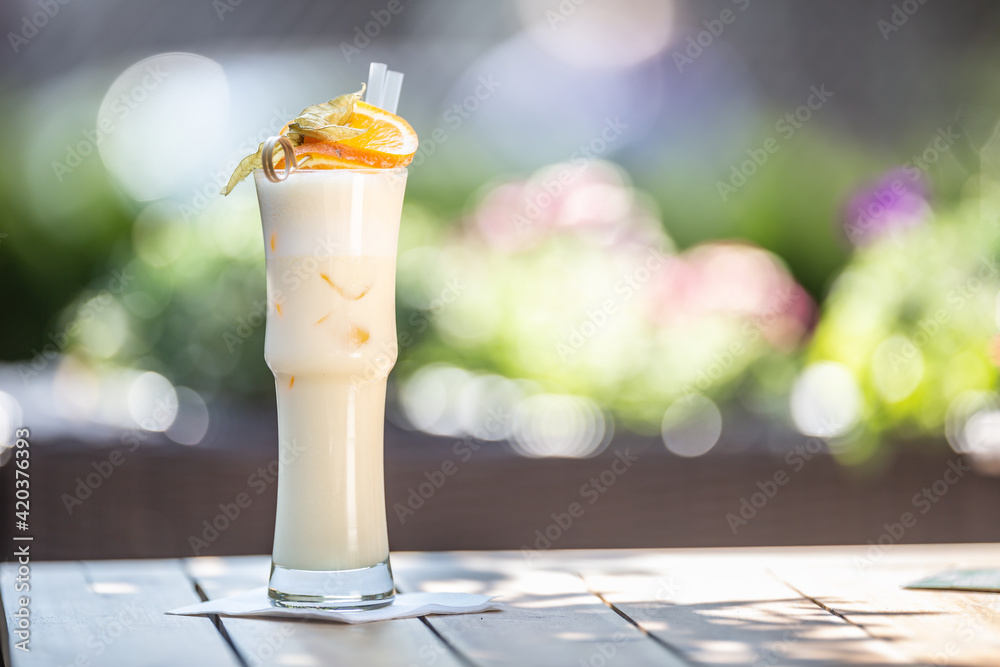 Sticker pinacolada cocktail with straws and orange on top served in a high glass on a summer terrace