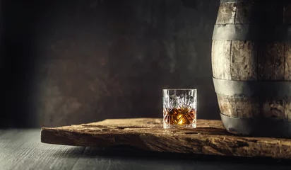 Fotobehang Glass of whisky or bourbon in ornamental glass next to a vinatge wooden barrel on a rustic wood and dark background © weyo