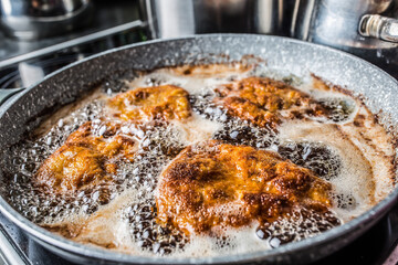 Schnitzels being fried in oil inside a dark pan