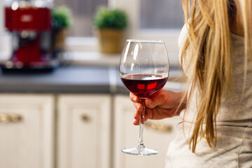 Unrecognizable blonde woman standing with glass of wine in kitchen