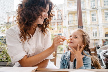 Mom and daughter eat french fries at an outdoor cafe