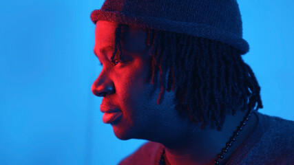 Pensive young african american black man lit with red and blue light. Close up face expression....
