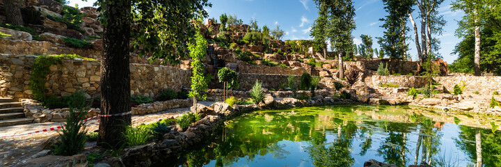 Fototapeta na wymiar Artificial pond or lake with a cascading fountain on a botanical park