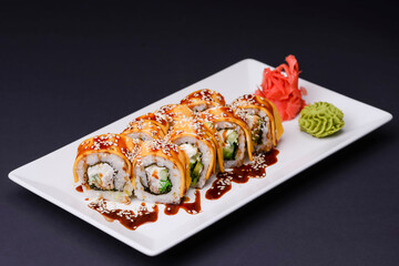 Eel, salmon and tuna sushi with unagi sauce served on a white plate over black background.