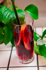 Pomegranate fruit cocktail drink in a tall glass with a plastic straw served over the white table with green leaves.