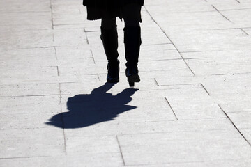 Black silhouette and shadow of lonely woman in boots walking on a street. Concept of loneliness, female fashion in early spring
