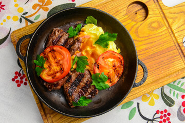 Close up of juicy beef steak served in a pan with bbq grilled tomatoes over traditional Ukrainian tablecloth.