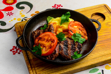 Close up of juicy beef steak served in a pan with bbq grilled tomatoes over traditional Ukrainian tablecloth.