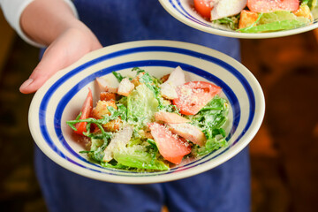 Caesar Salad served by waiter in a restaurant or diner. Two plates of traditional caesar salad. Italian cuisine concept.