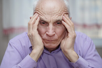 Older greyhaired man holds head with hand for headache disease.