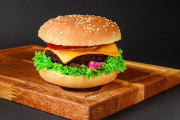 Bacon and beef patty burger with red onions and cheese over black background. Fast food, junk food concept.