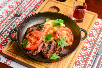 Close up of juicy beef steak served in a pan with bbq grilled tomatoes over traditional Ukrainian tablecloth.