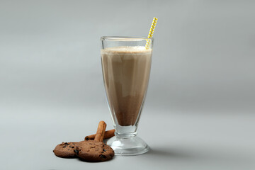 Glass of chocolate milkshake, cookies and cinnamon on gray background