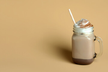 Glass of chocolate milkshake with straw on beige background