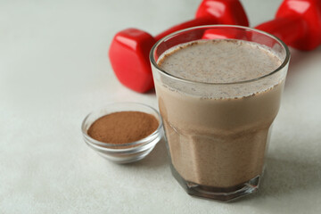 Chocolate milkshake, chocolate powder and dumbbells on white textured table