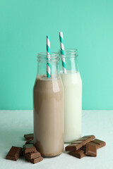 Bottles with milk and milkshake, and chocolate pieces against mint background