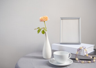 Beautiful rose flower in modern white vase with mock up  silver frame,book and coffee cup decoration with Amethyst and Quartz necklace on linen cloth table in room interior