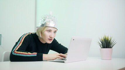 Crazy woman typing on laptop with foil hat to shields her from 5G waves, internet, electromagnetic...