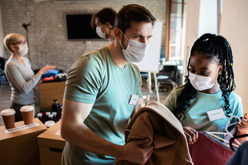 Group of volunteers with face mask working in community charity donation center.