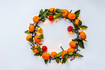 Christmas wreath of lighting garland, tangerines and little christmas balls on the white background. Christmas decorations. Holiday and celebration concept. Copy space.