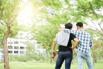 Rear view of two young friends standing with beer and talking outdoors