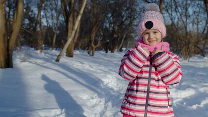 Joyful little child girl smiling, showing thumbs up gesture on snowy road in winter park outdoors