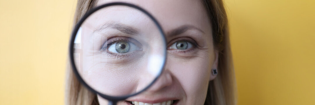 Young woman holding magnifying glass near her eye