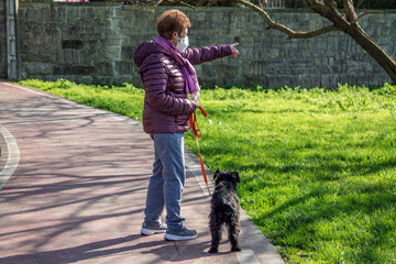 Portrait of senior woman with disposable medical mask and her dog walking outside