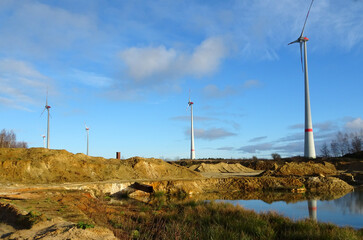 Wind turbines beside a sand excavation. The reflection of one of the windmills in the water