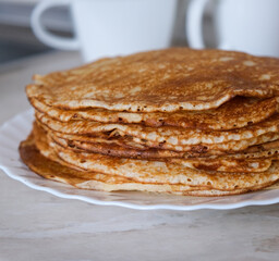 Stack of thin crepes, blini with butter on white plate. Maslenitsa, Shrove Tuesday concept. Vertical orientation, rustic style