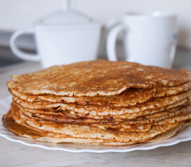 Stack of thin crepes, blini with butter on white plate. Maslenitsa, Shrove Tuesday concept. Vertical orientation, rustic style